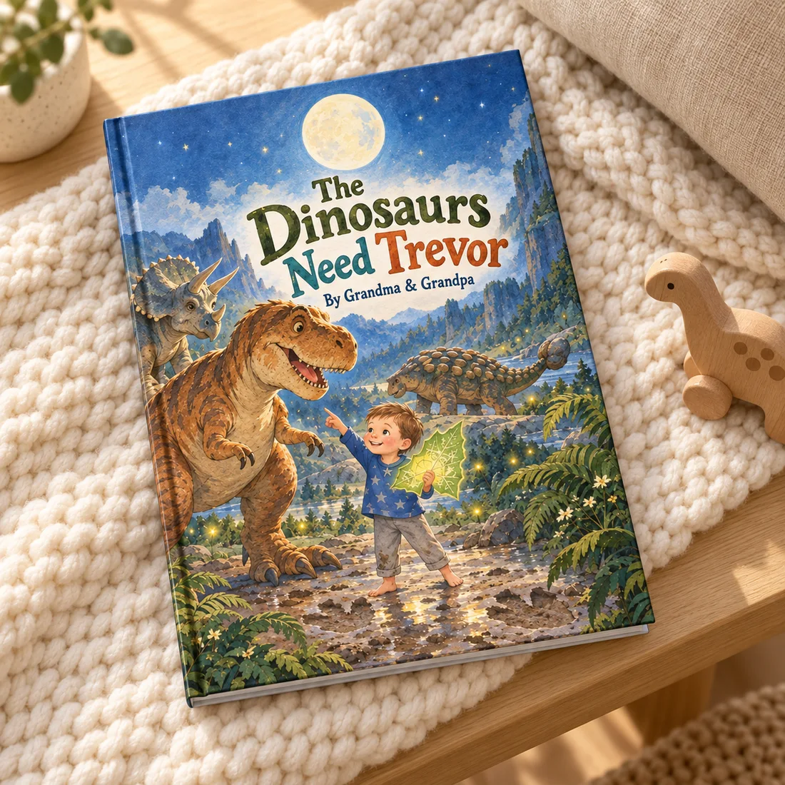 The Dinosaurs Need Trevor — styled mockup of the hardcover on an ivory knit blanket