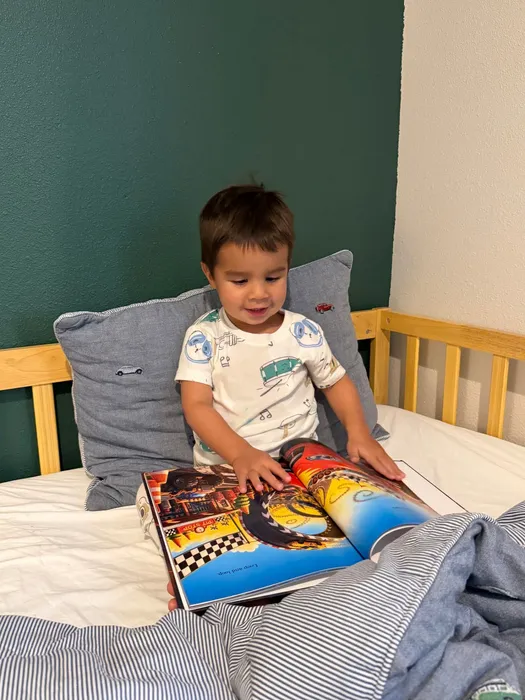 A two-year-old tucked into bed, absorbed in a personalized hardcover storybook.