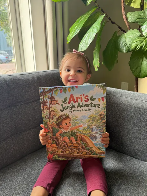A smiling child holding Ari’s Jungle Adventure on a sofa