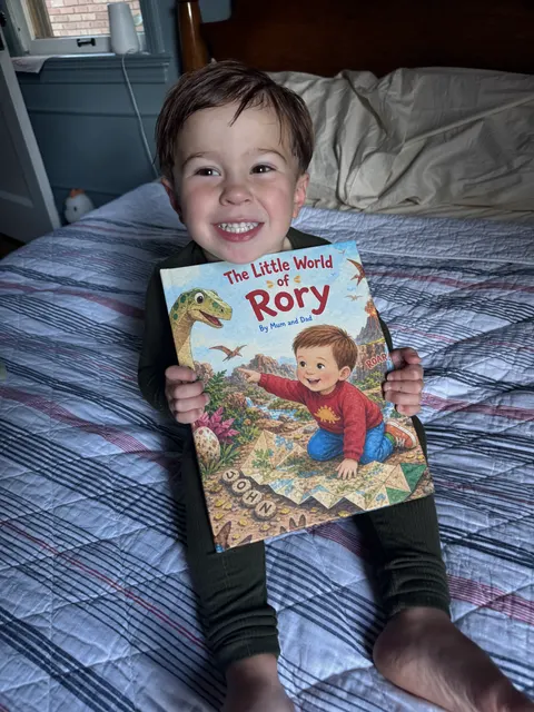 A smiling child holding The Little World of Rory on a bed