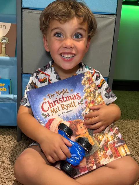 A smiling child holding The Night Christmas Met Ryatt and a blue toy truck