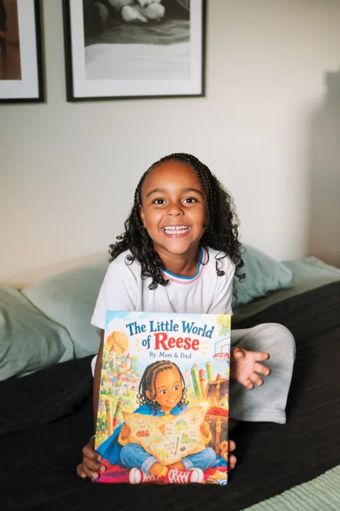 A smiling child holding The Little World of Reese on a bed