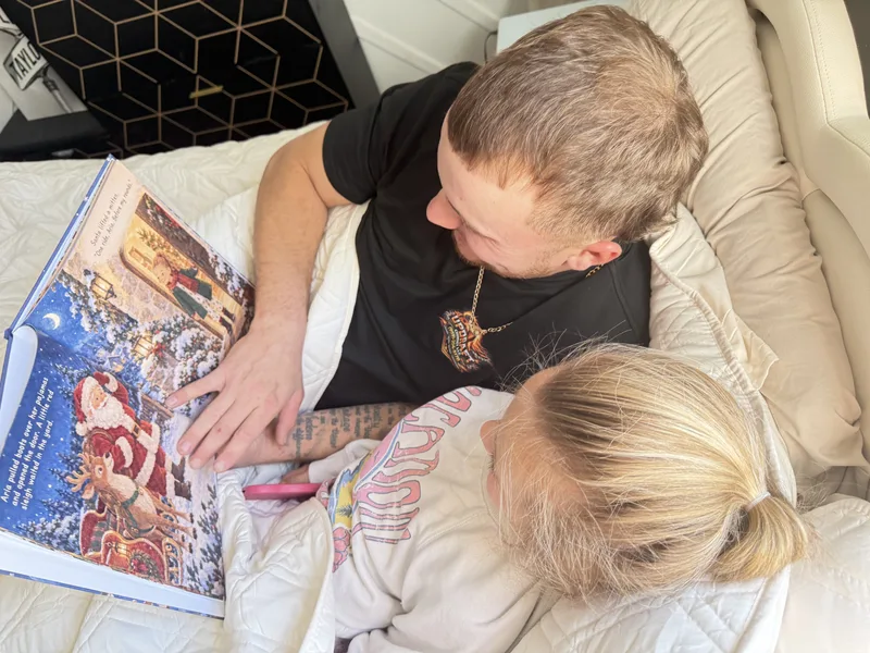 A parent and child reading a printed Sundayfawn Christmas book, open to an illustrated Santa and reindeer spread