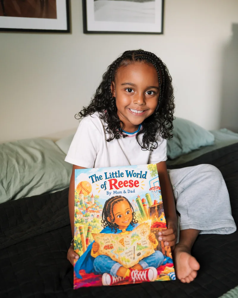 Reese smiling and holding her printed book The Little World of Reese, by Mom and Dad
