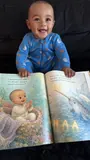 Vihaan smiling behind an open personalized newborn storybook.